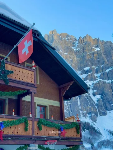 Schweizer Flagge an einem Chalet unter verschneiter Felswand
