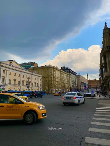 Autos und gelbes Taxi auf einer Stadtstraße unter Wolken