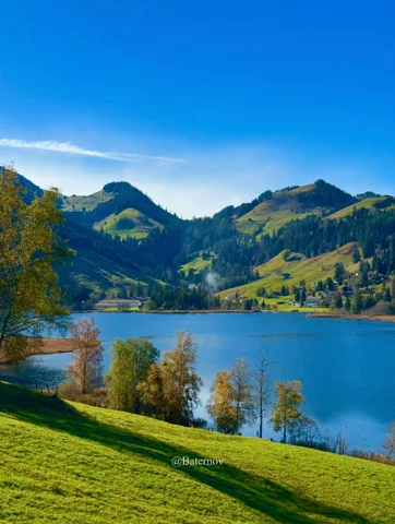 Blauer See zwischen grünen Hügeln und verstreuten Häusern