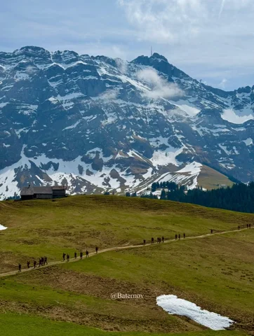 Offene Bergweide unter verschneiten Felsen
