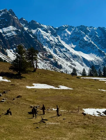 Menschen auf einer Bergwiese unter Schneegipfeln